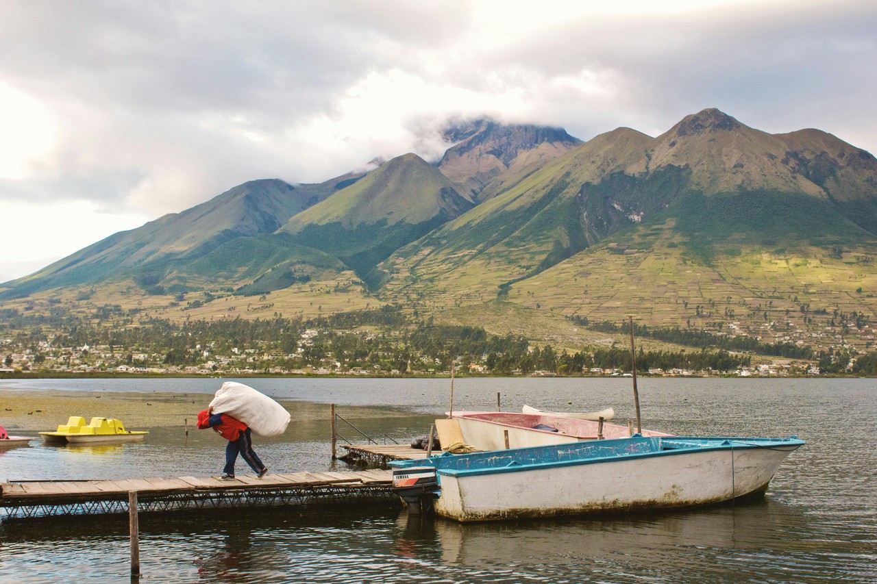 Laguna andina ecuatoriana con botes tradicionales y volcán de fondo